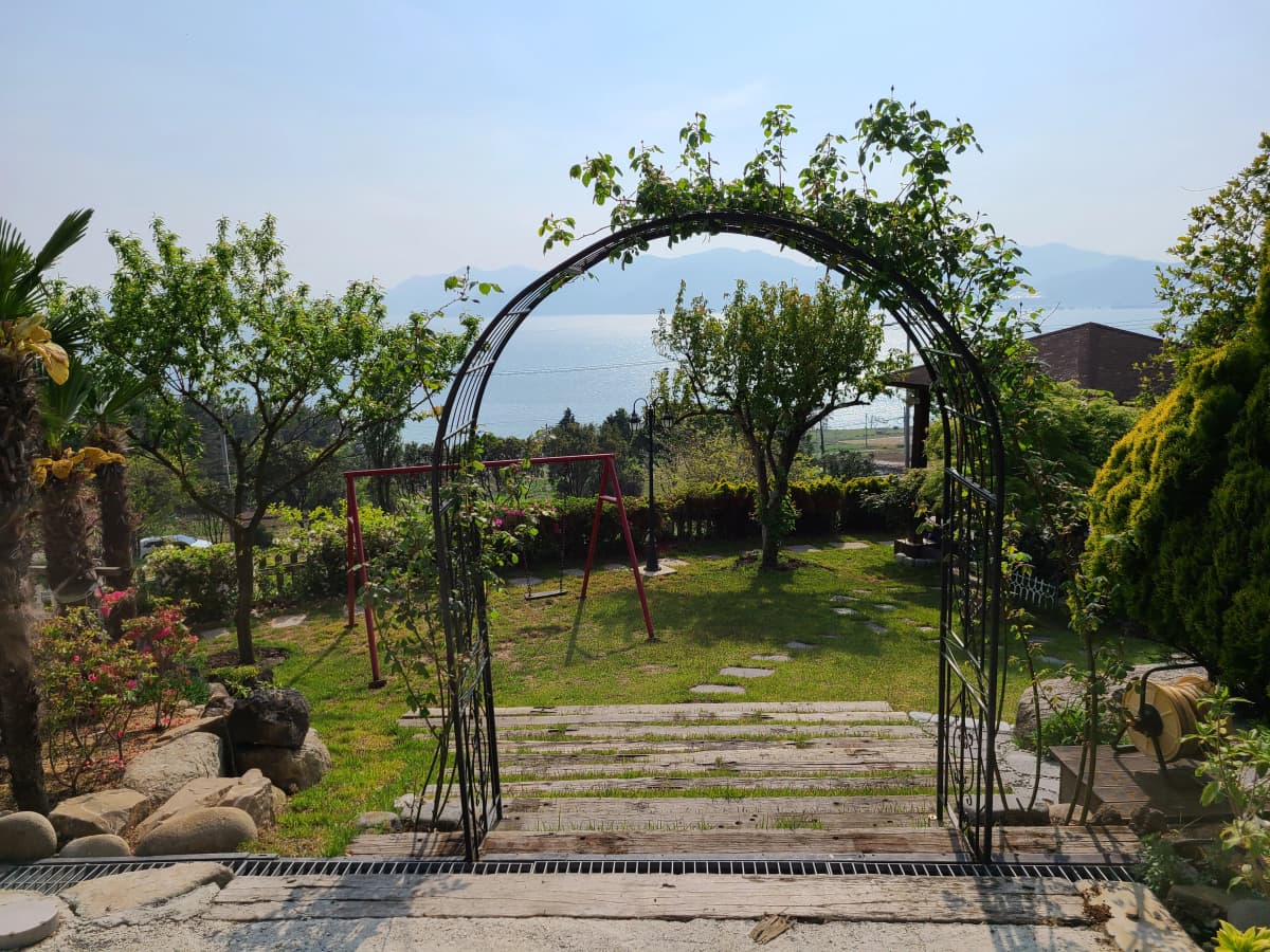 하늘빛바다펜션 봄 낮 아치 너머로 바다가 펼쳐지는 정원 길